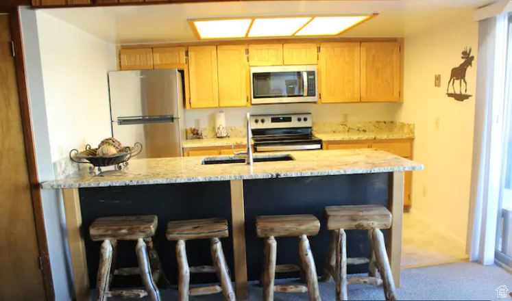 Kitchen with appliances with stainless steel finishes, a kitchen bar, and light stone counters