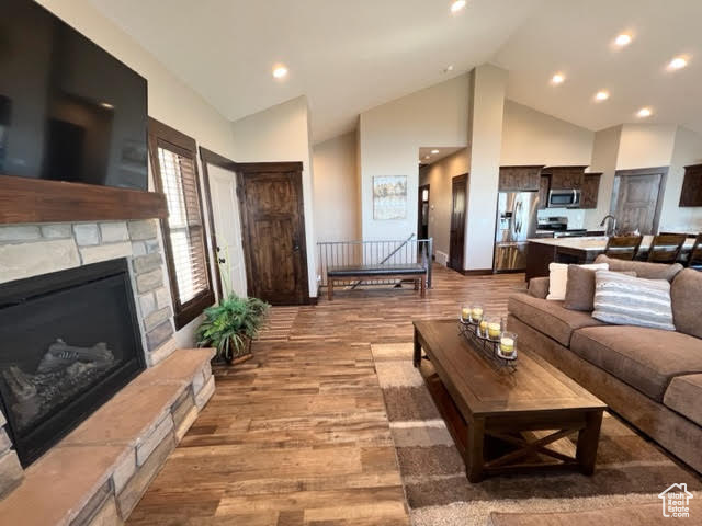 Living room with high vaulted ceiling, light wood-type flooring, and a stone fireplace