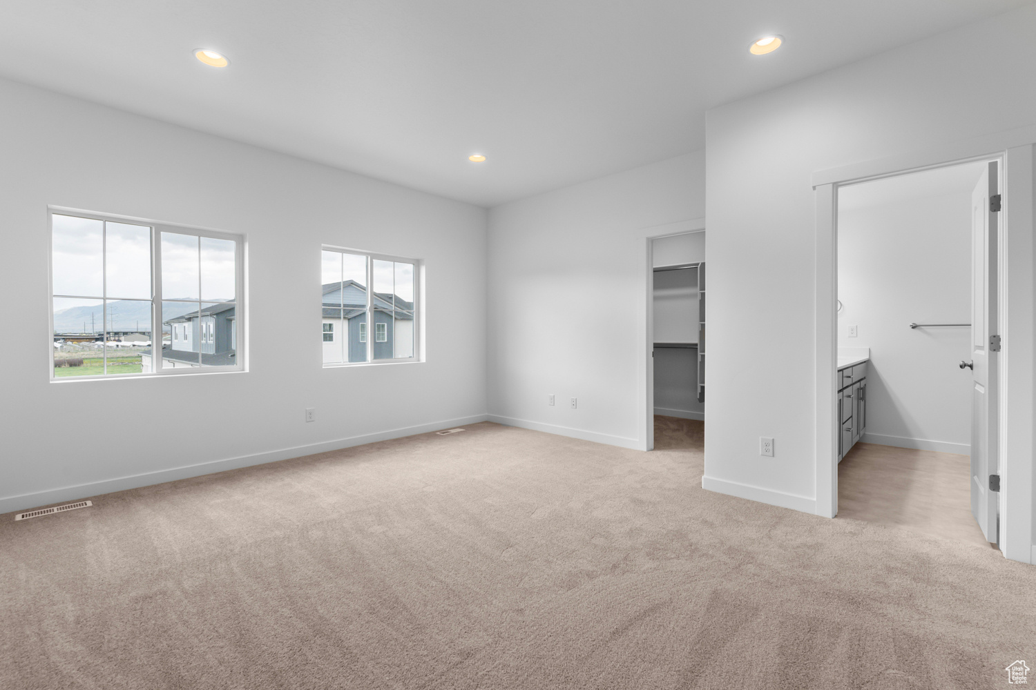 Unfurnished bedroom featuring a walk in closet, light carpet, and connected bathroom