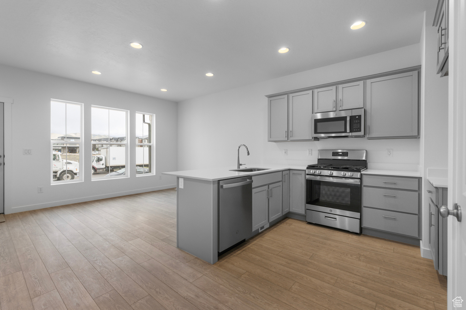 Kitchen with light wood-type flooring, gray cabinetry, kitchen peninsula, stainless steel appliances, and sink