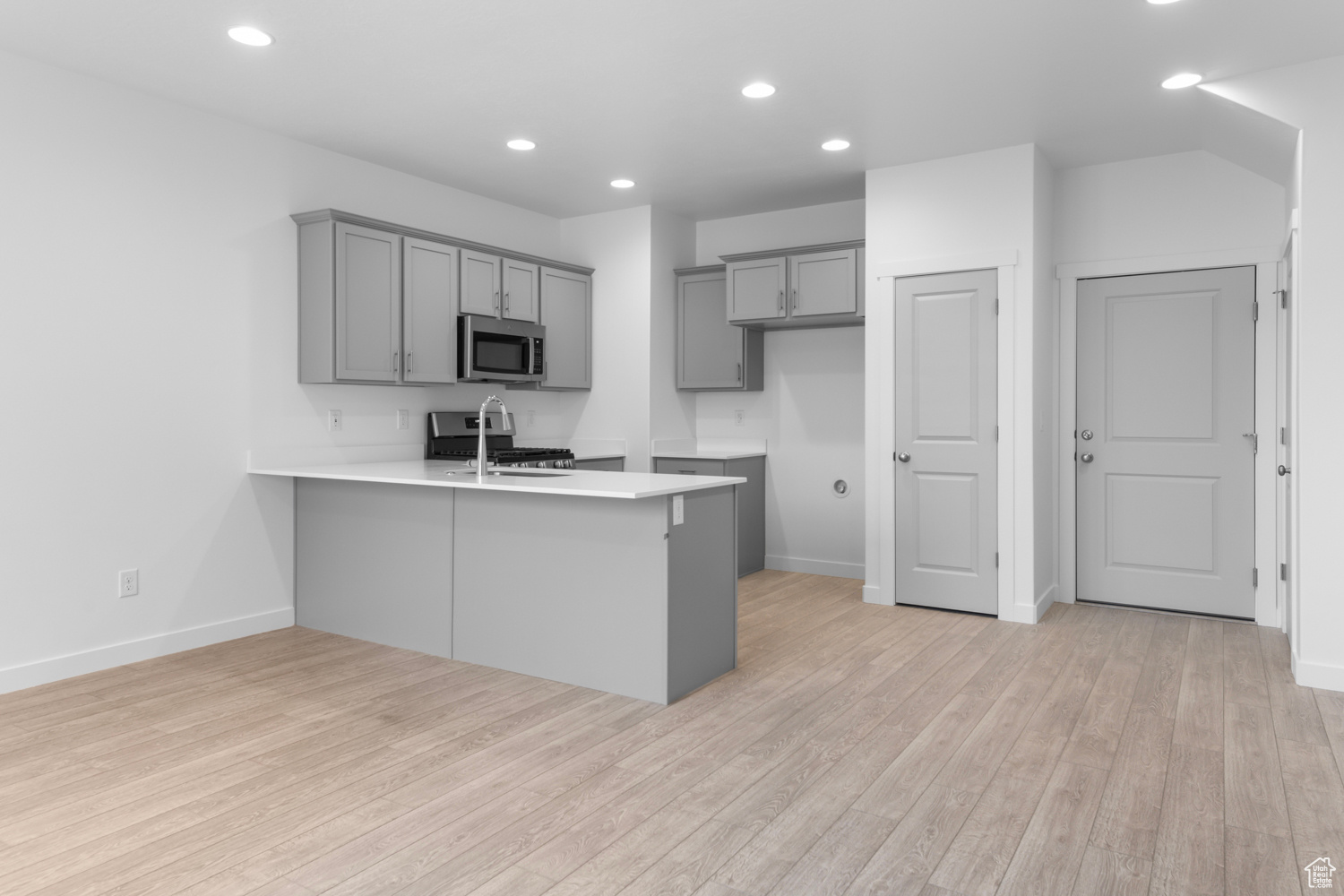 Kitchen featuring range with gas cooktop, light hardwood / wood-style floors, kitchen peninsula, and gray cabinets