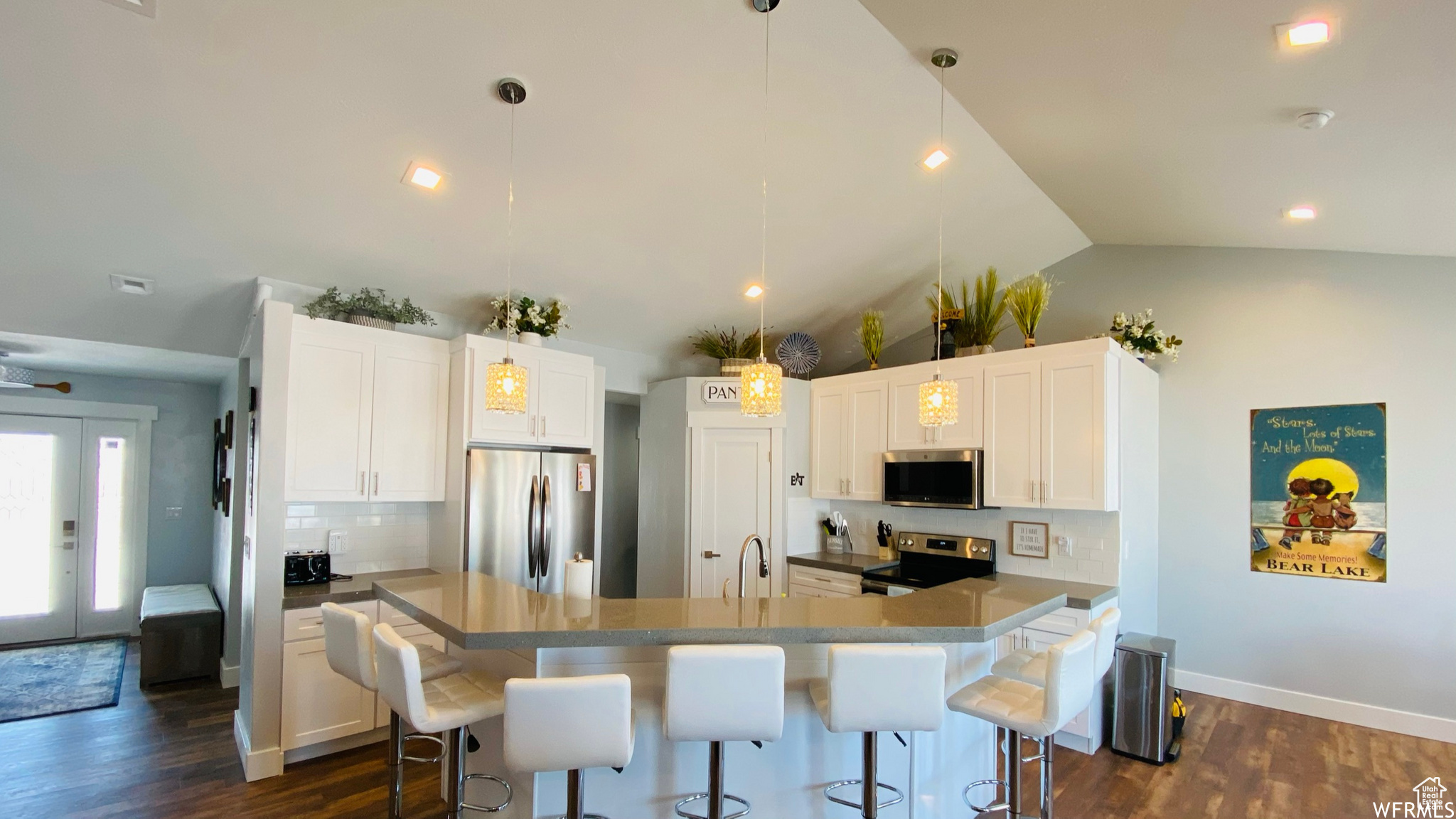 Kitchen featuring dark hardwood / wood-style floors, white cabinets, decorative light fixtures, an island with sink, and appliances with stainless steel finishes