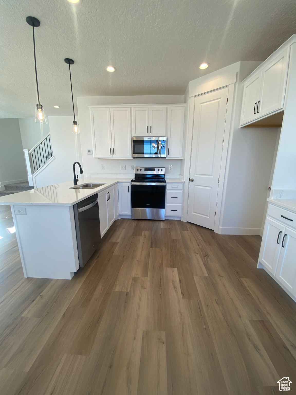 Kitchen with sink, dark wood-type flooring, appliances with stainless steel finishes, white cabinetry, and decorative light fixtures. Pictures are for reference only of the MAINE floor plan. Actual finishes may vary.