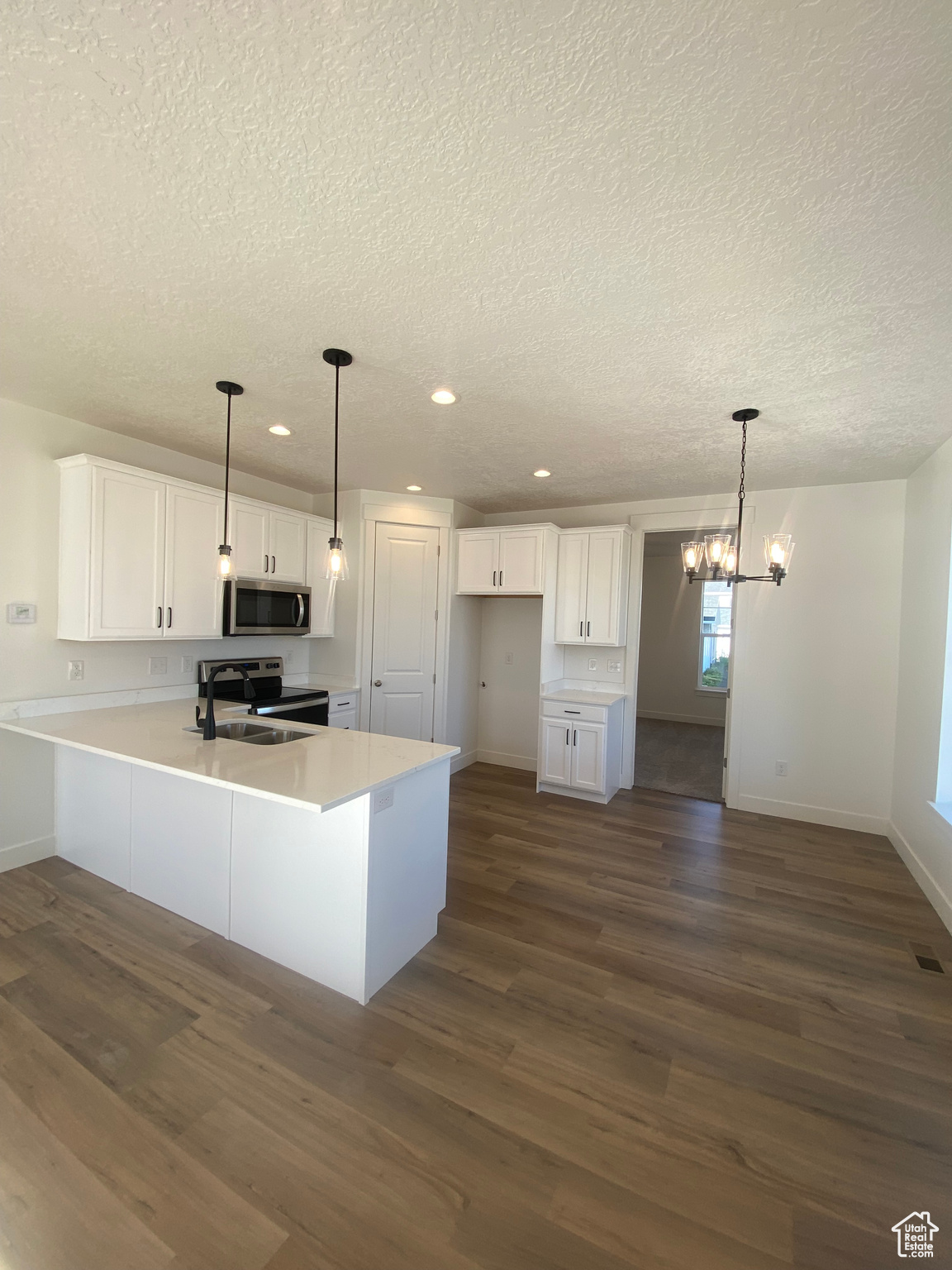 Kitchen with appliances with stainless steel finishes, dark hardwood / wood-style floors, a textured ceiling, white cabinets, and decorative light fixtures.  Pictures are for reference only of the MAINE floor plan. Actual finishes may vary.