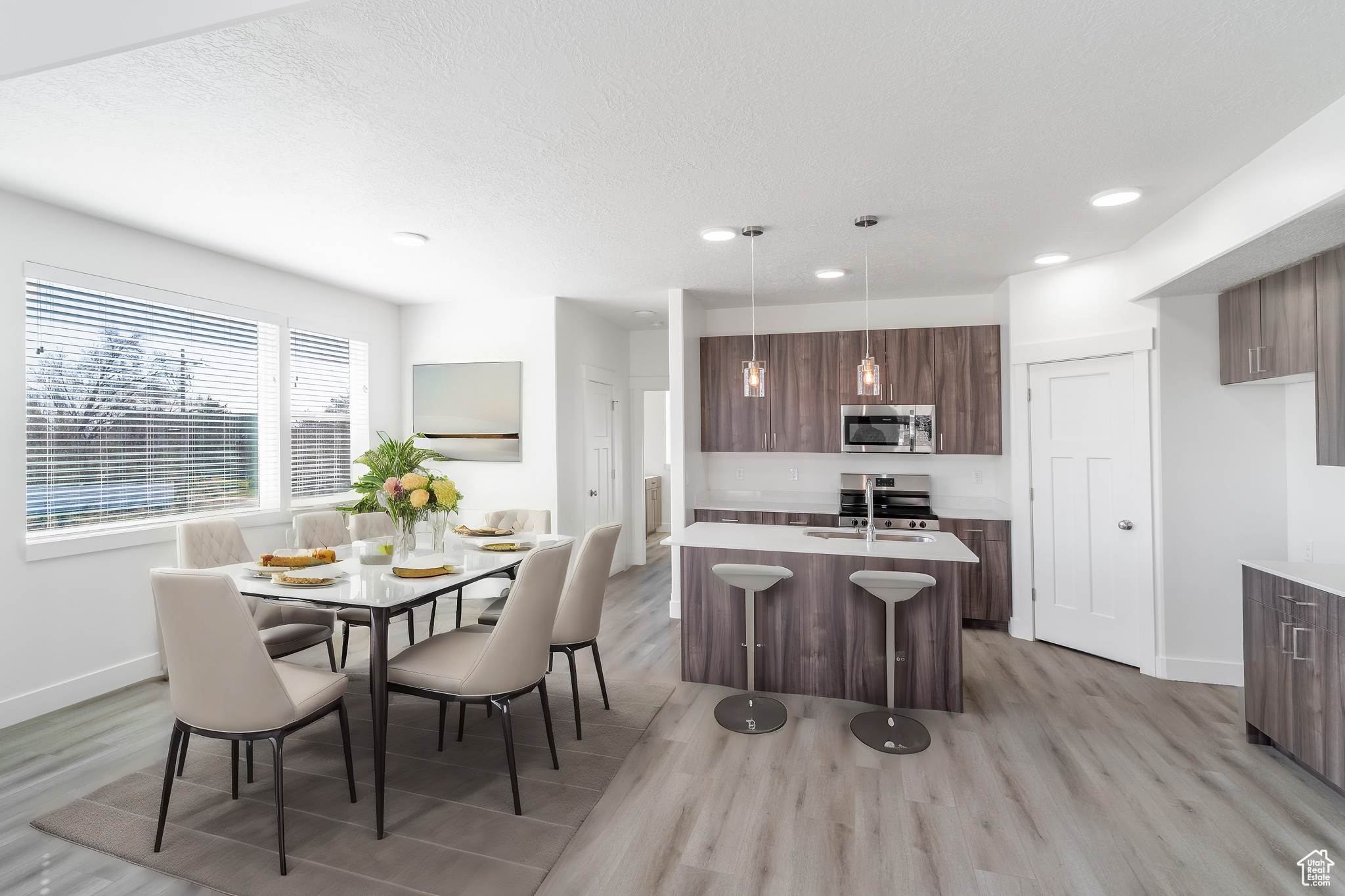 Kitchen with appliances with stainless steel finishes, dark brown cabinetry, a center island with sink, hanging light fixtures, and light hardwood / wood-style floors