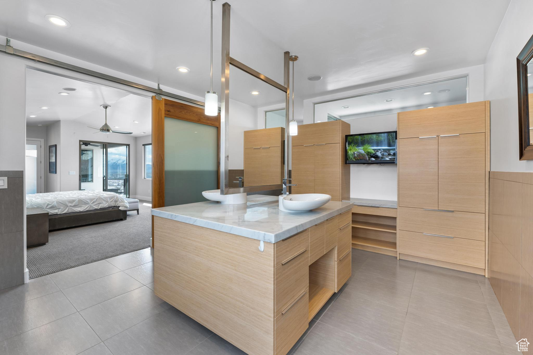 Kitchen with light tile flooring, a kitchen island with sink, sink, light stone countertops, and ceiling fan