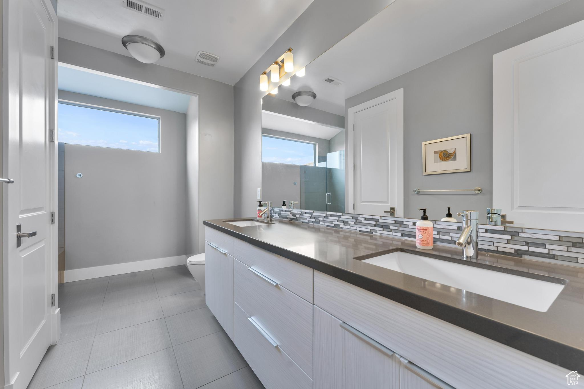 Bathroom featuring dual vanity, toilet, tasteful backsplash, and tile flooring