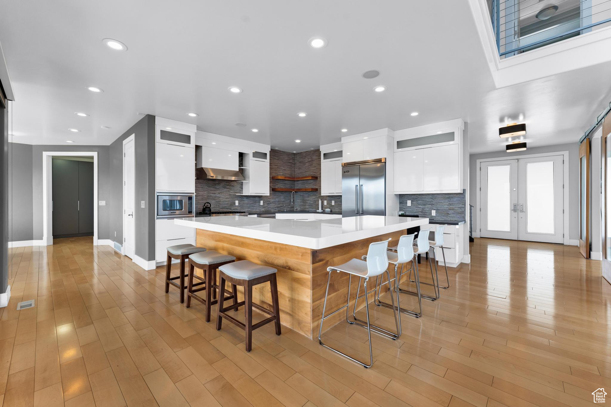 Kitchen featuring wall chimney range hood, white cabinetry, french doors, built in appliances, and a kitchen bar