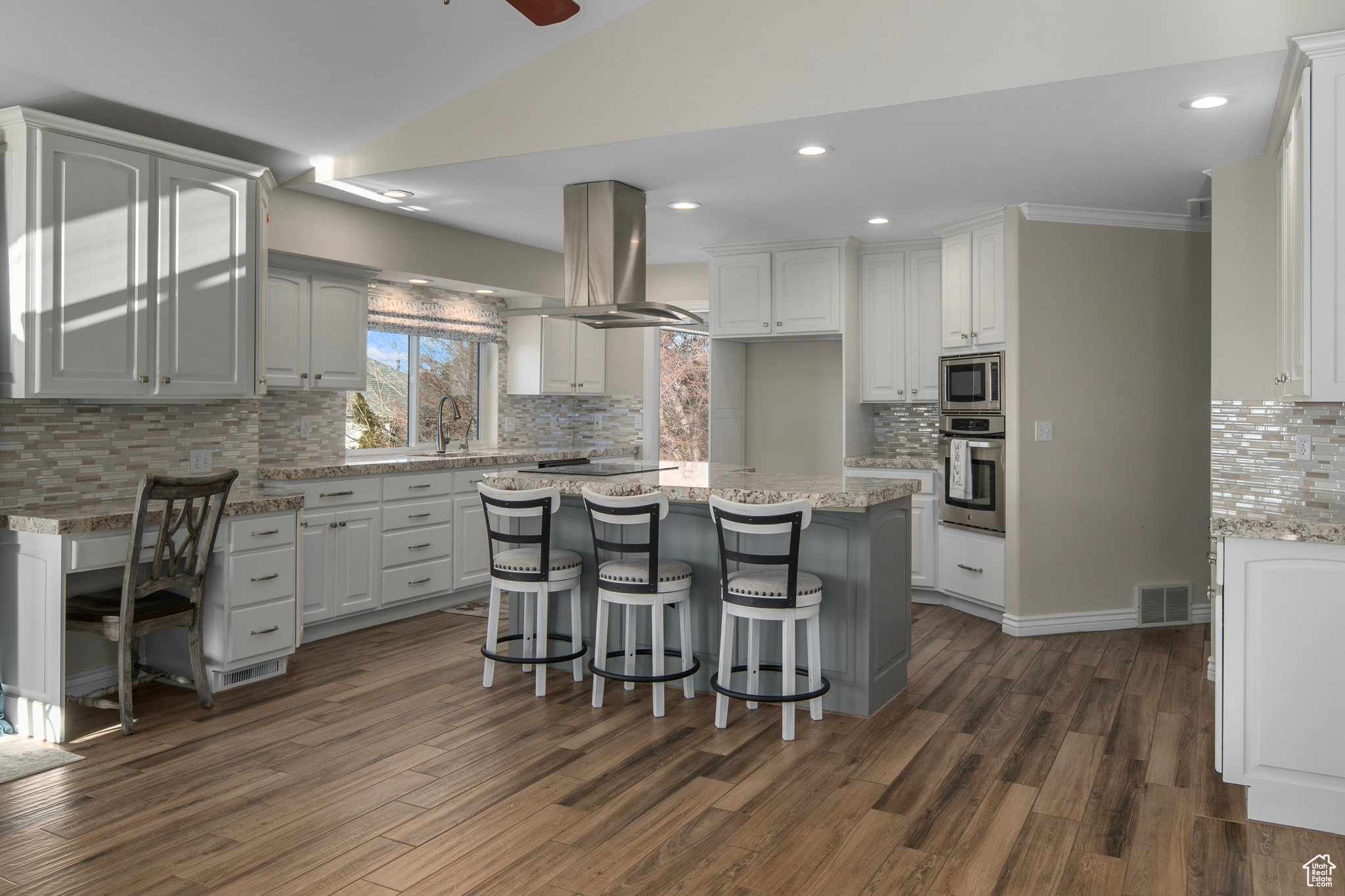 Kitchen featuring a kitchen breakfast bar, ceiling fan, appliances with stainless steel finishes, white cabinets, and island range hood