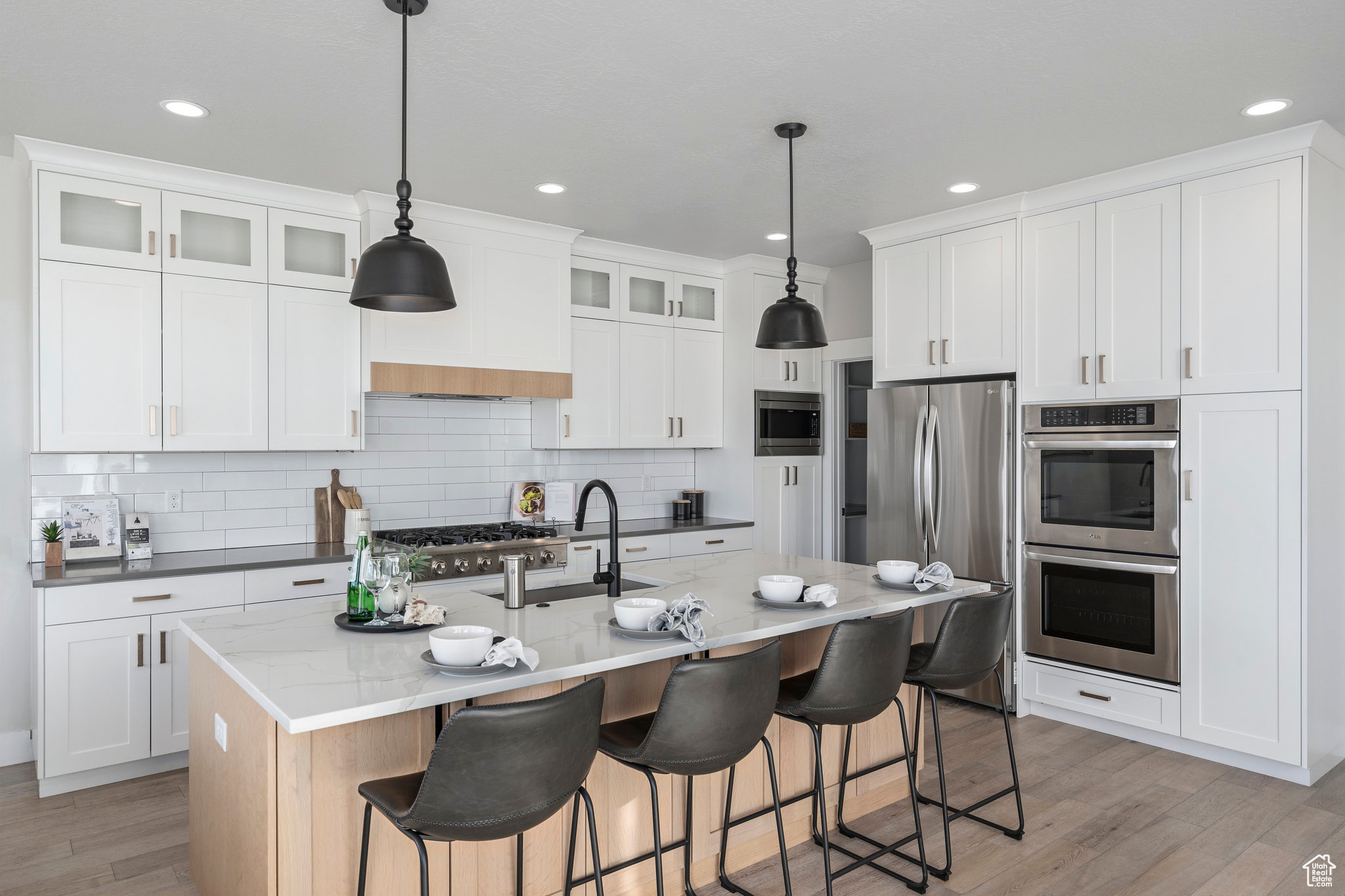 Kitchen featuring a kitchen island with sink, appliances with stainless steel finishes, white cabinetry, and decorative light fixtures