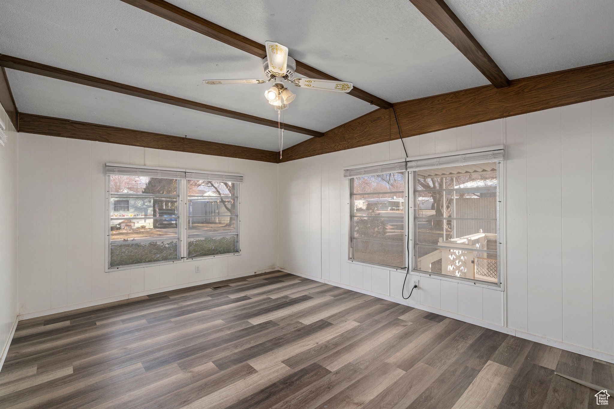 Empty room with dark hardwood / wood-style floors, ceiling fan, and lofted ceiling with beams