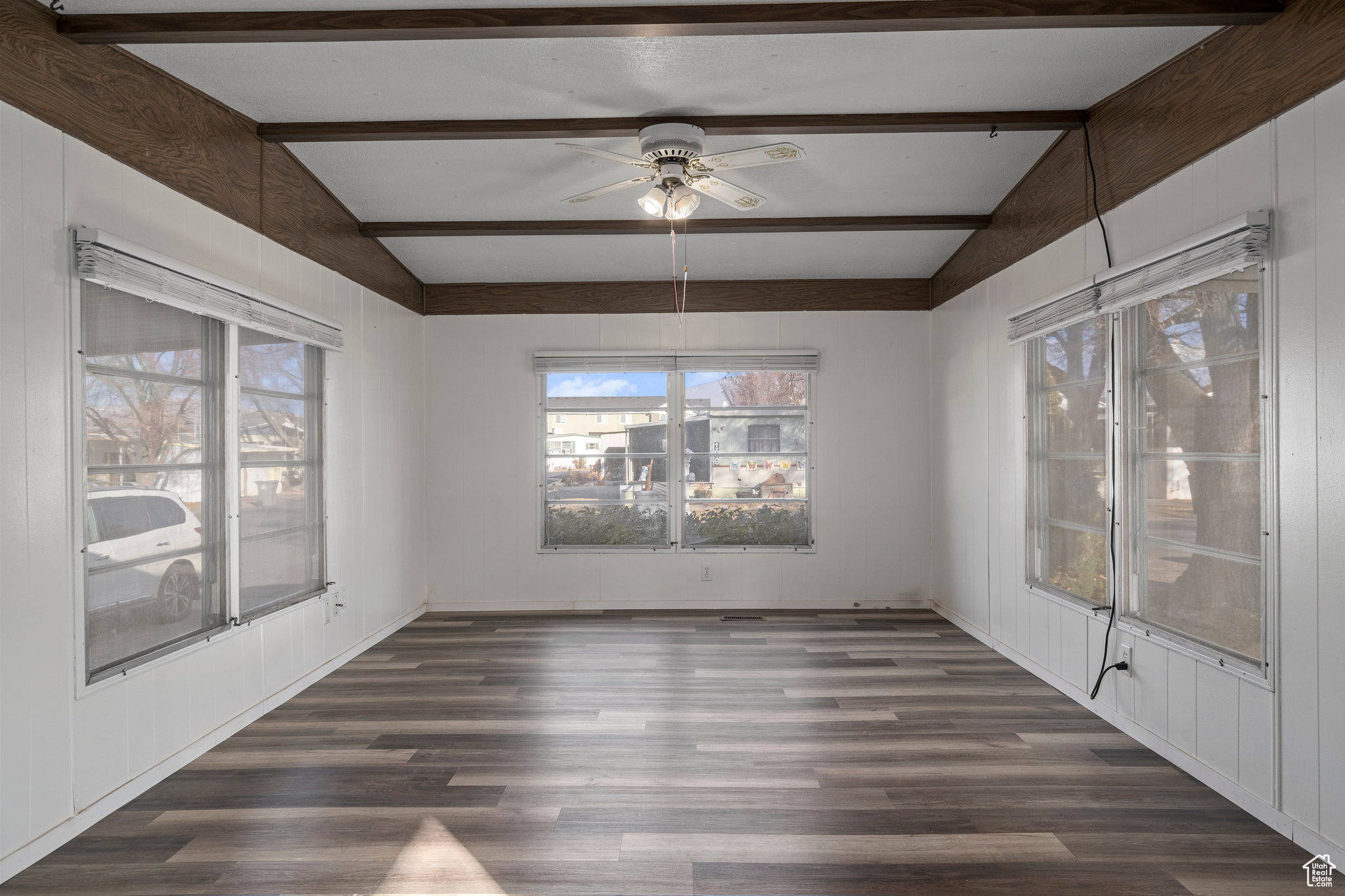 Empty room with lofted ceiling with beams, dark hardwood / wood-style floors, and ceiling fan