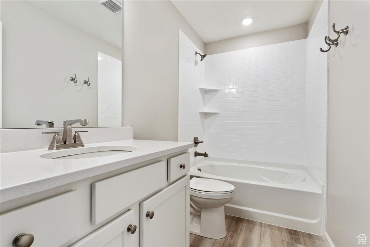 Full bathroom with toilet, tiled shower / bath, vanity, and hardwood / wood-style flooring