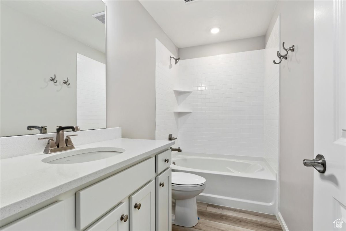 Full bathroom with hardwood / wood-style floors, vanity, toilet, and tiled shower / bath