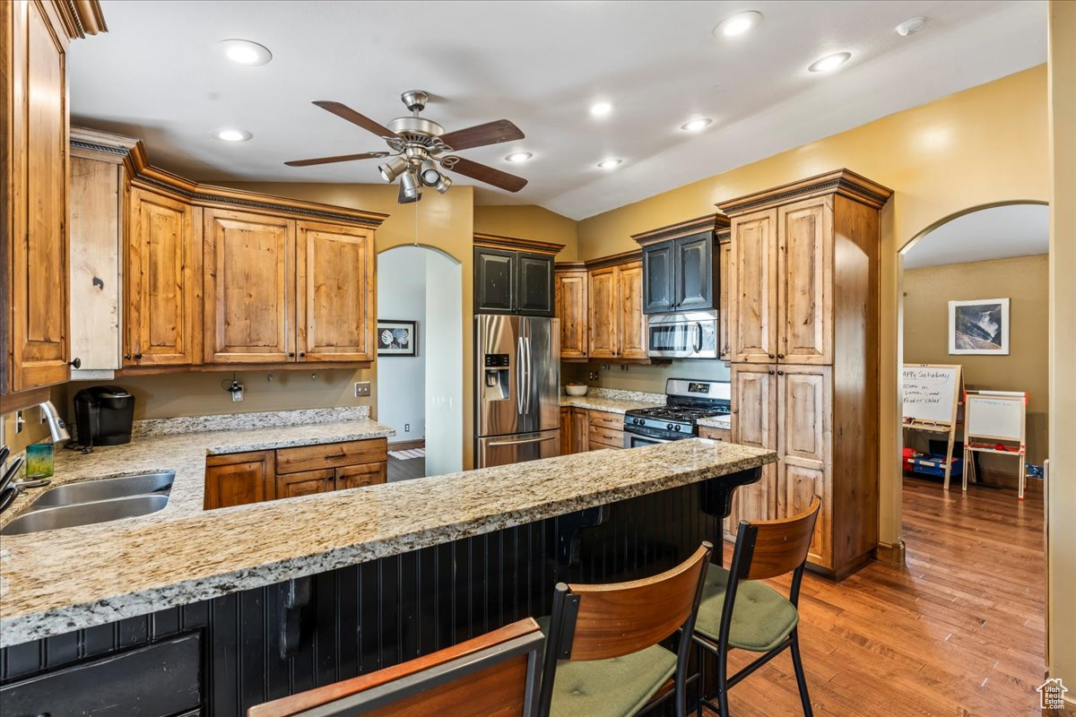 Kitchen featuring a kitchen breakfast bar, ceiling fan, sink, light hardwood / wood-style floors, and stainless steel appliances