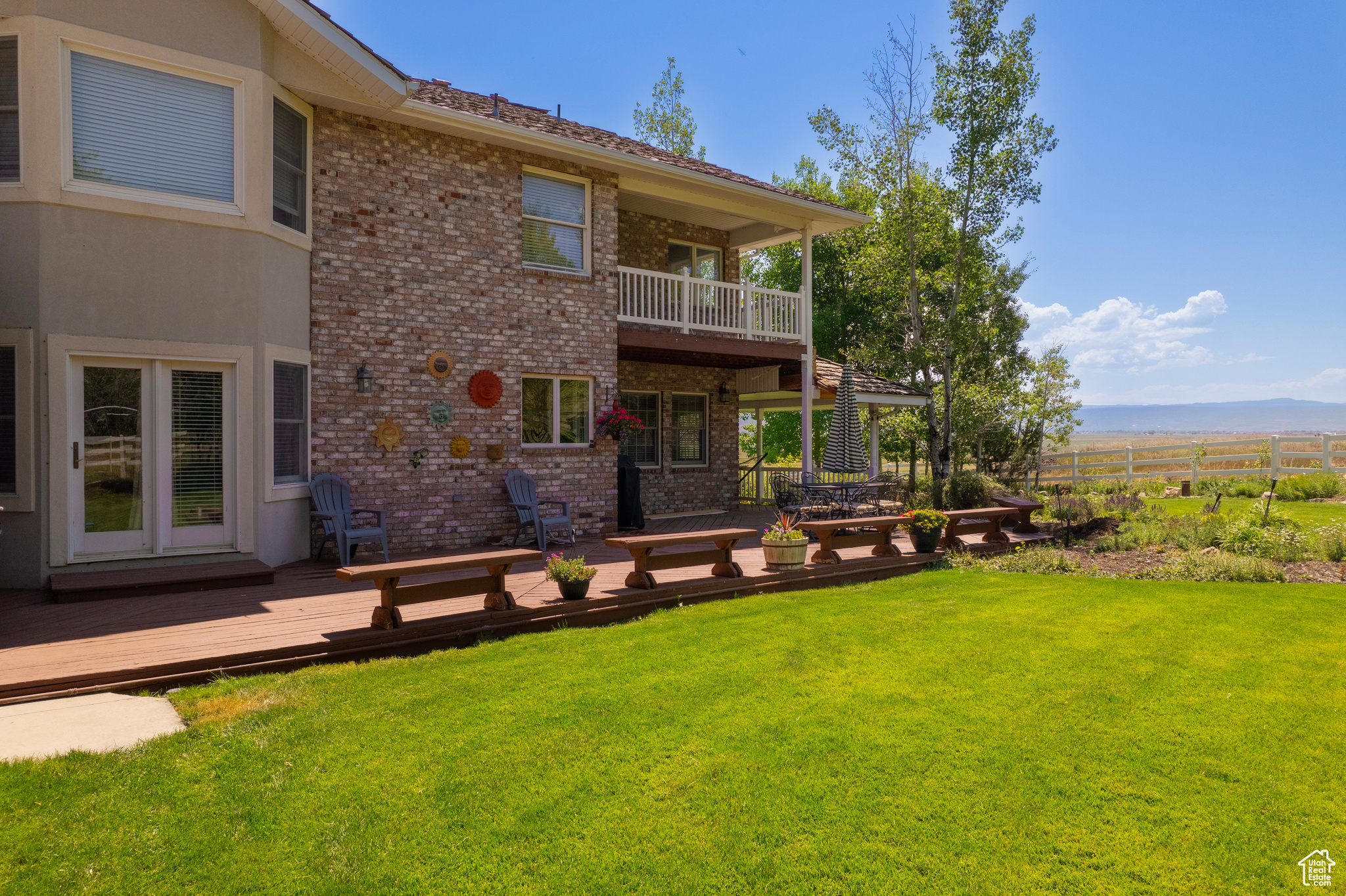 Rear view of property featuring a balcony, a yard, and a wooden deck