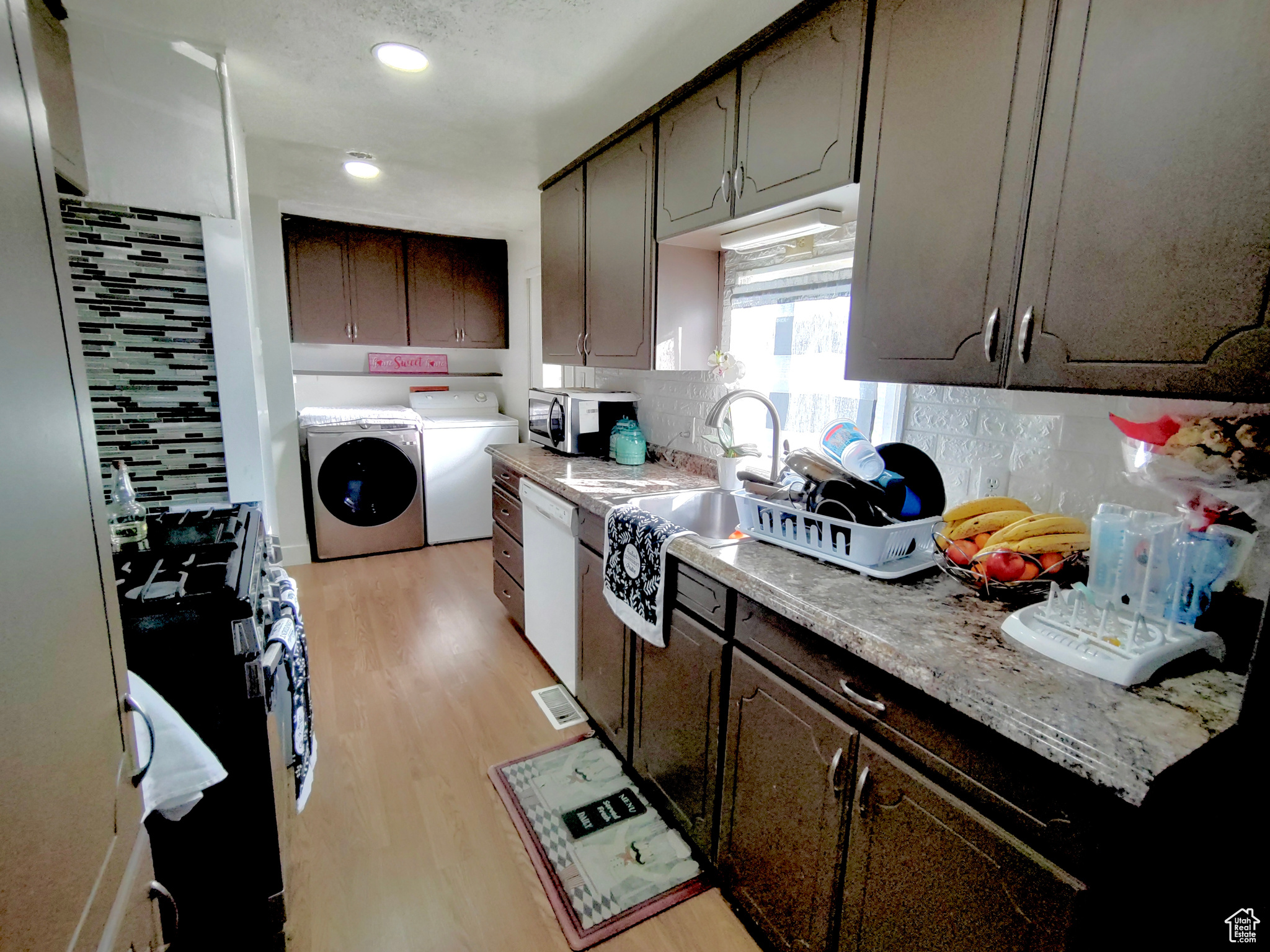 Kitchen with washing machine and clothes dryer, range, light hardwood / wood-style flooring, backsplash, and dark brown cabinets