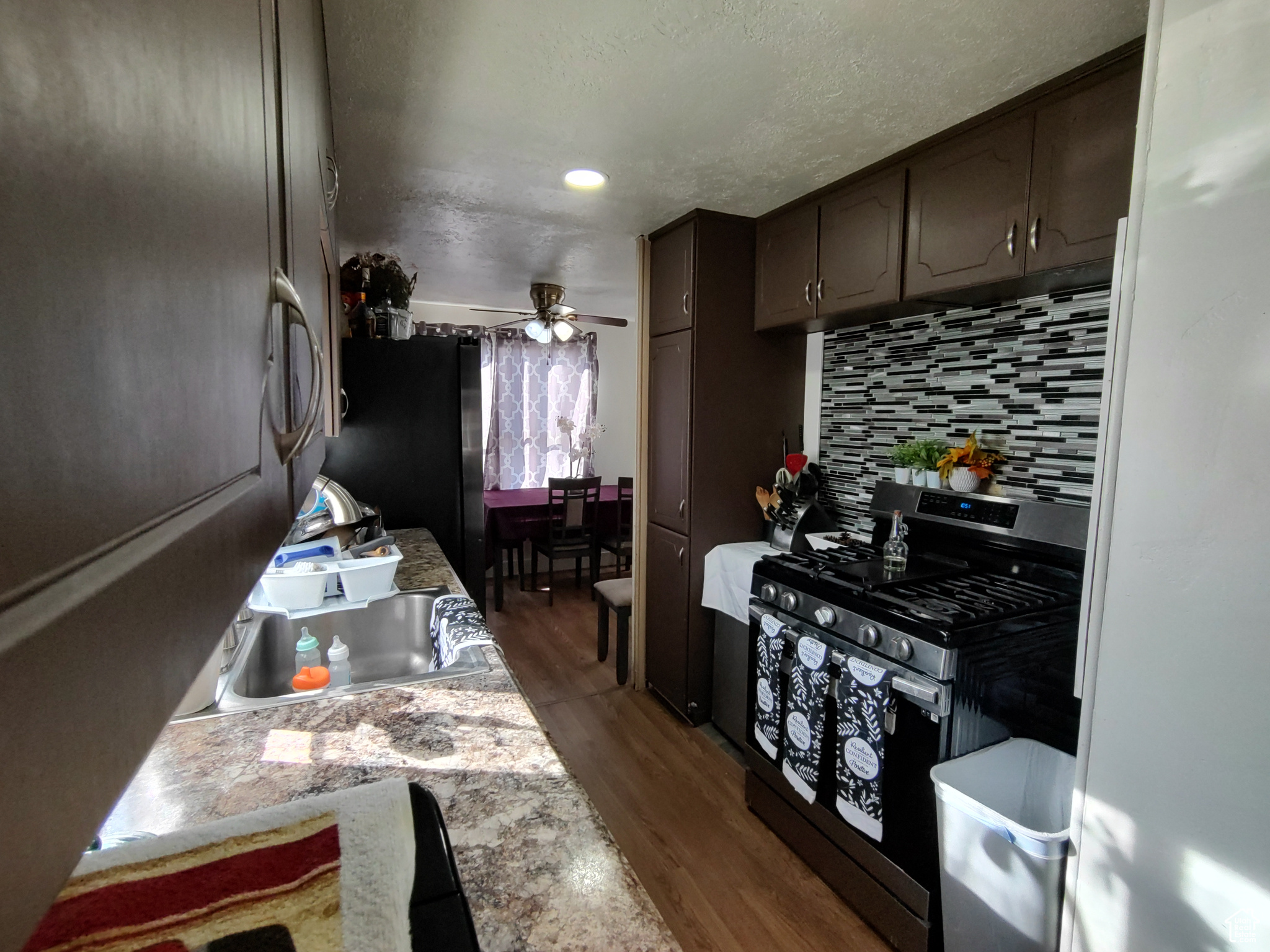 Kitchen with tasteful backsplash, hardwood / wood-style floors, ceiling fan, gas stove, and dark brown cabinetry