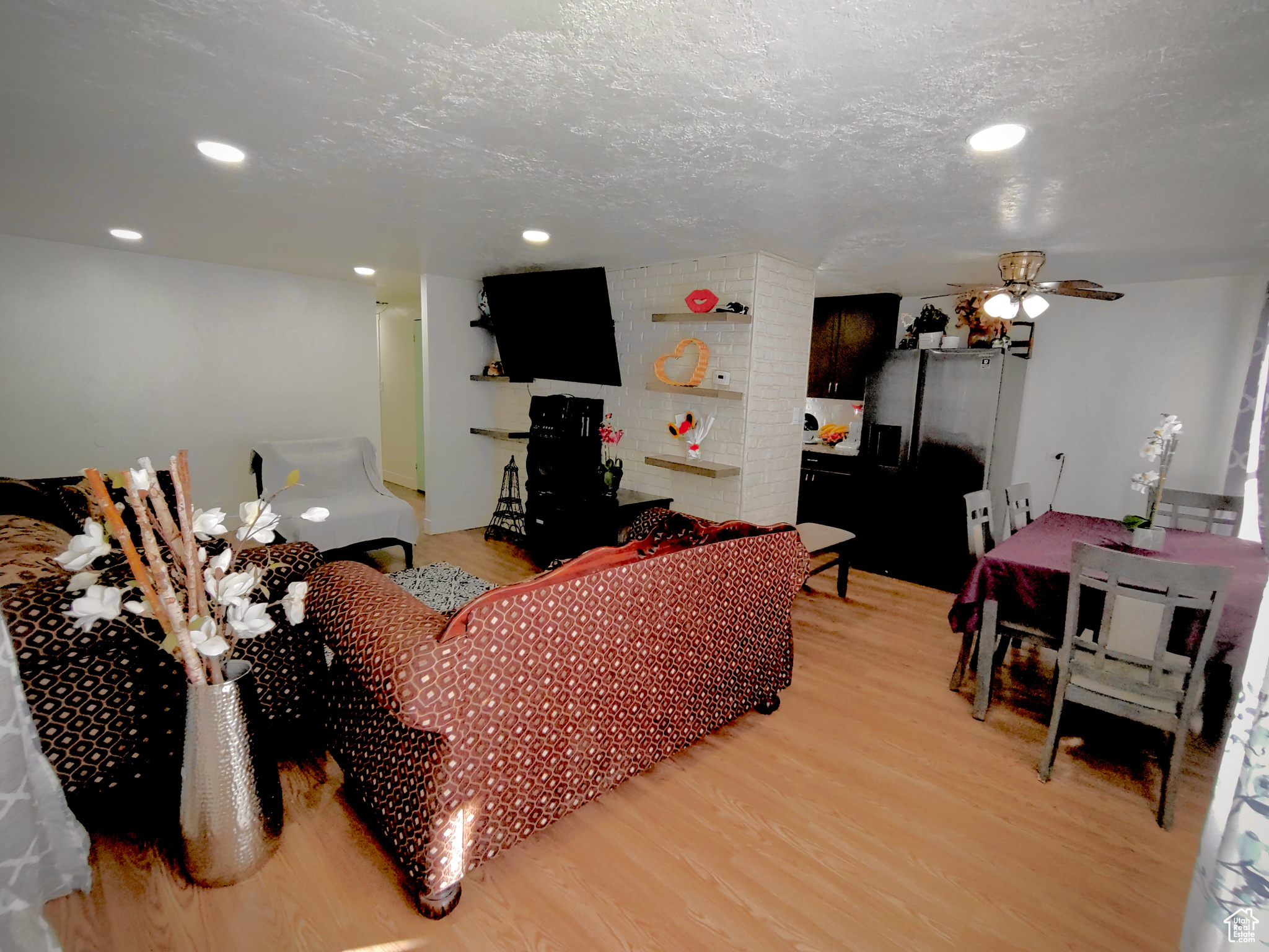 Living room featuring brick wall, a textured ceiling, light hardwood / wood-style floors, and ceiling fan