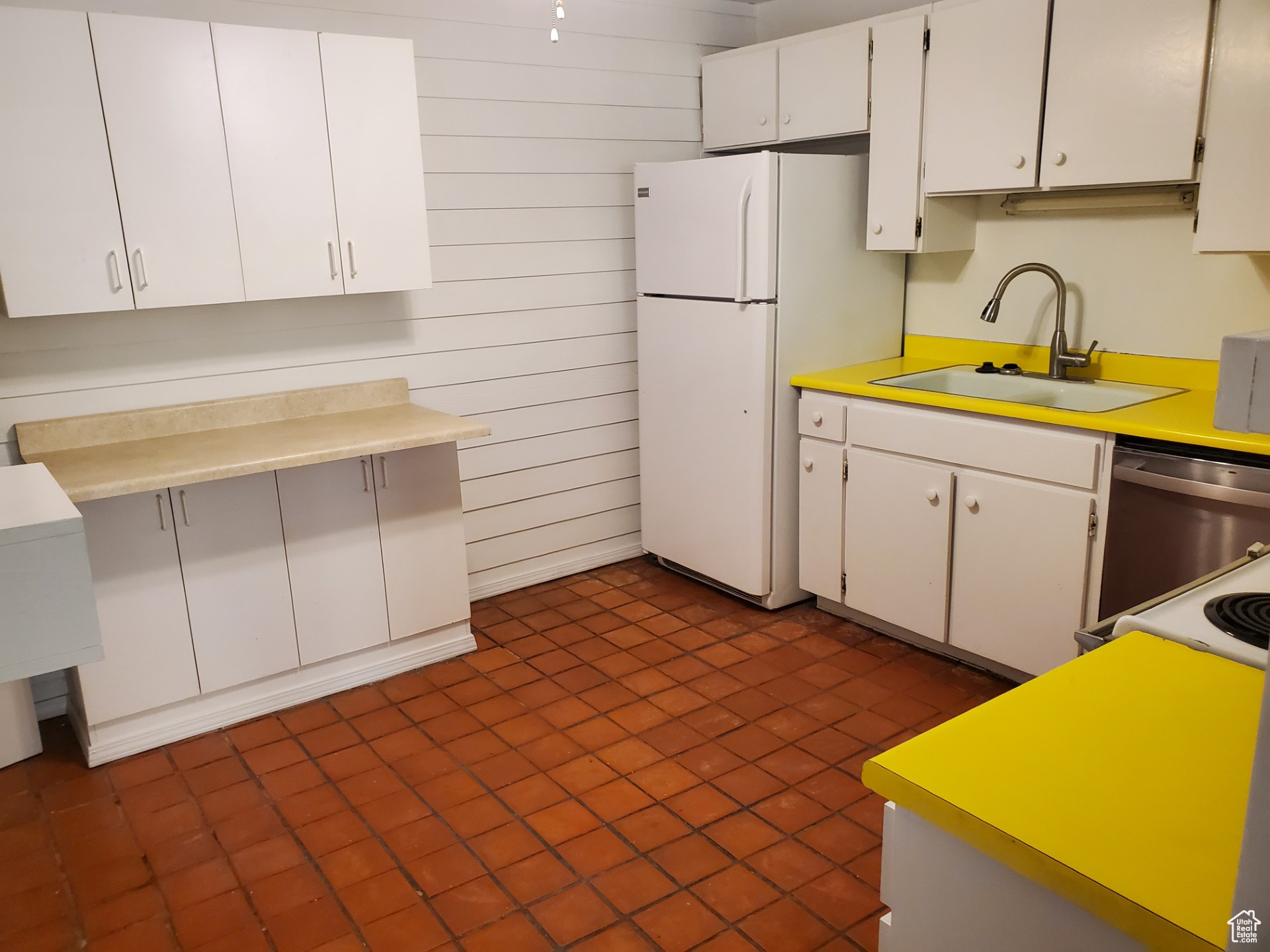 Kitchen featuring dark tile flooring, white refrigerator, dishwasher, sink, and white cabinetry