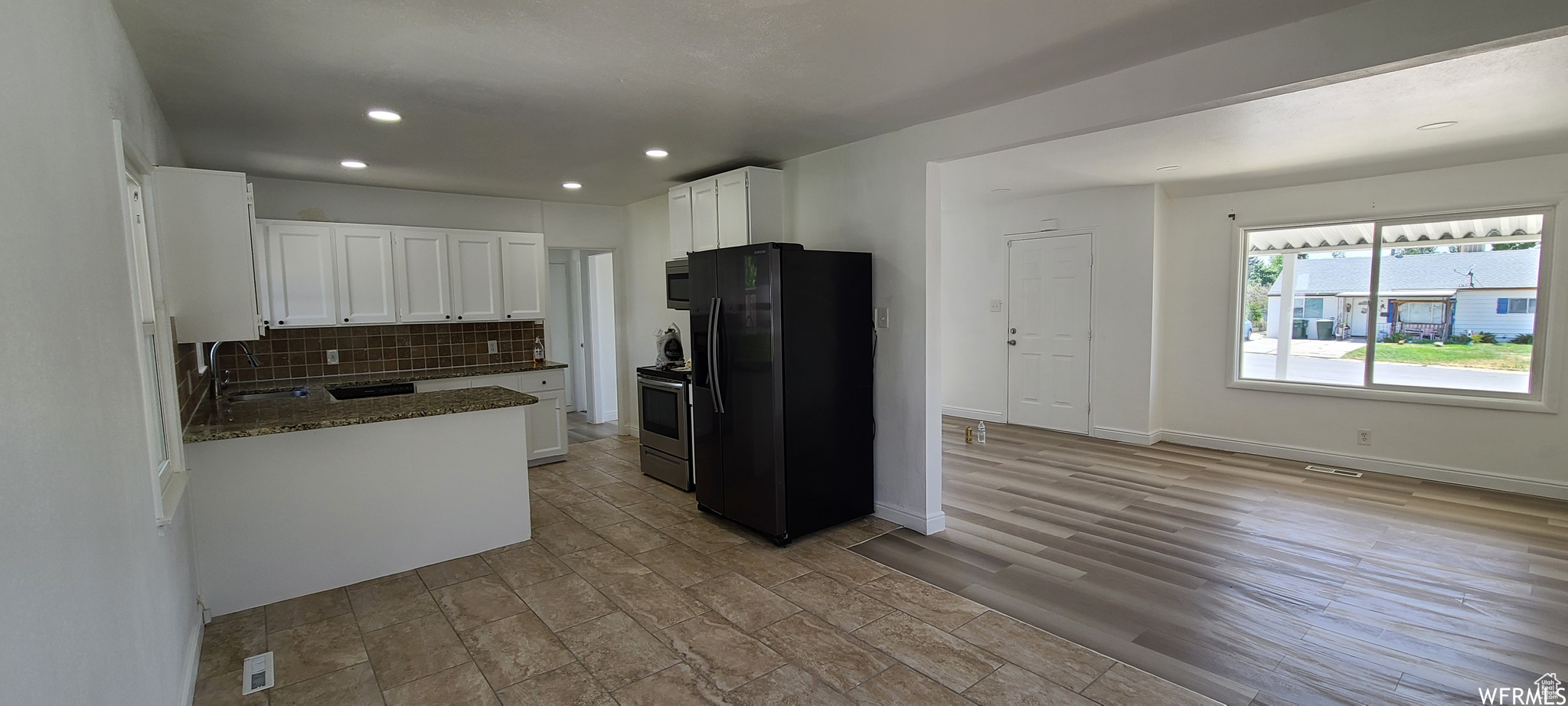 Kitchen featuring appliances with stainless steel finishes, white cabinetry, light tile flooring, dark stone counters, and backsplash