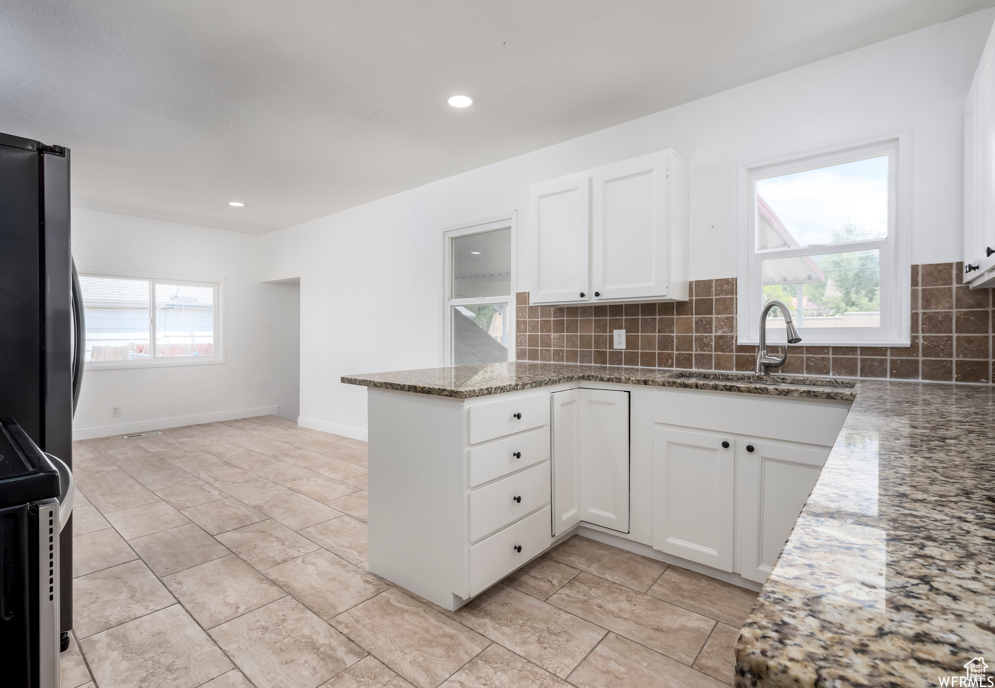 Kitchen featuring backsplash, white cabinetry, light tile floors, and stone countertops