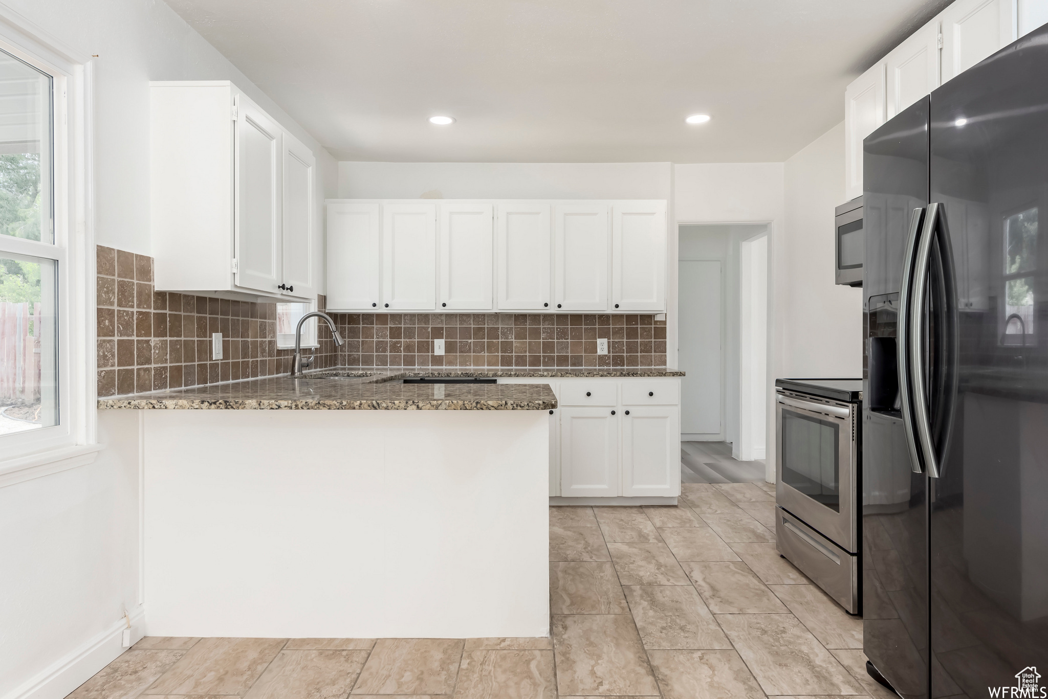 Kitchen with tasteful backsplash, stone countertops, stainless steel appliances, and white cabinetry