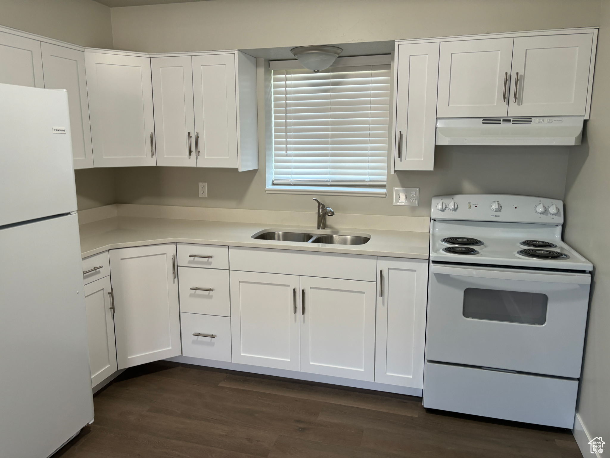 Kitchen featuring white cabinetry, sink, white appliances, and dark hardwood / wood-style floors