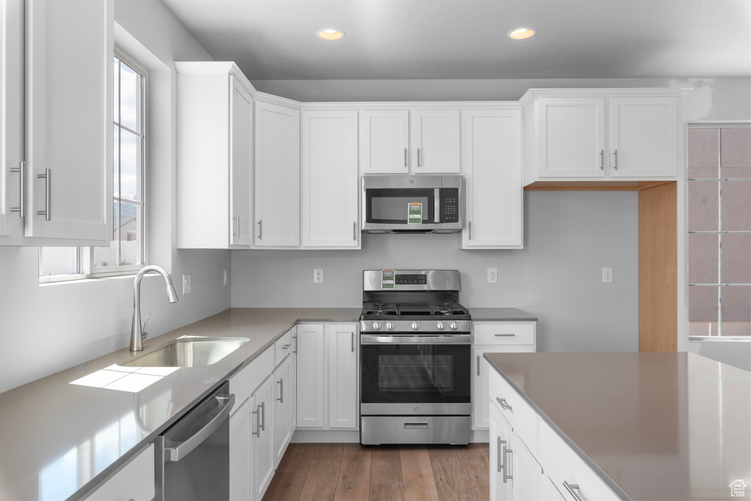 Kitchen with sink, white cabinets, hardwood / wood-style floors, and stainless steel appliances