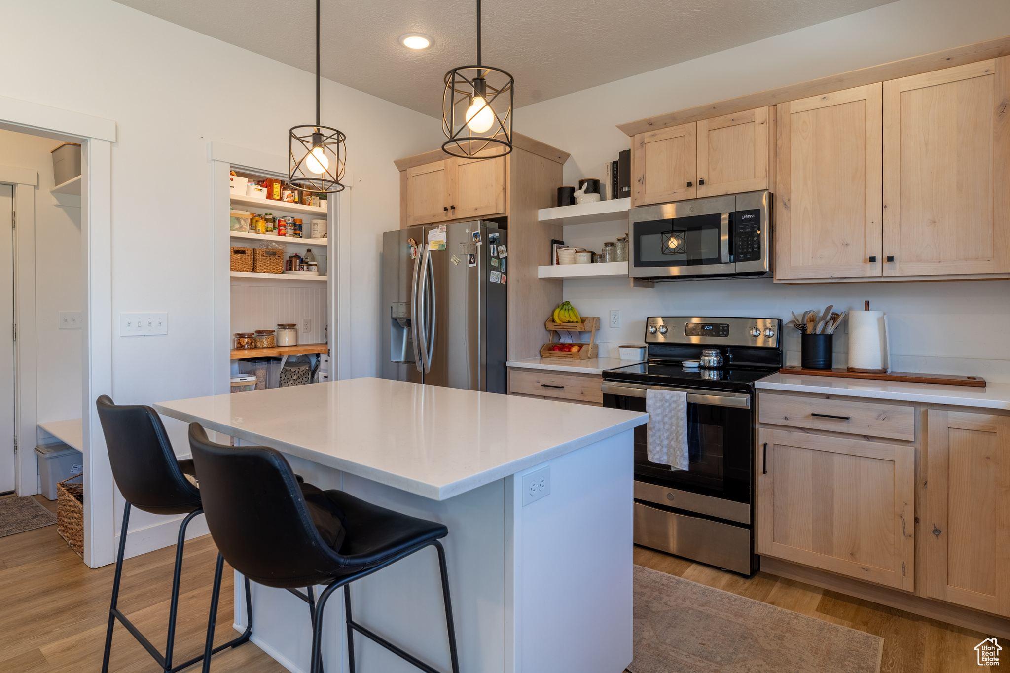 Kitchen featuring a kitchen breakfast bar, pendant lighting, appliances with stainless steel finishes, light hardwood / wood-style flooring, and light brown cabinetry