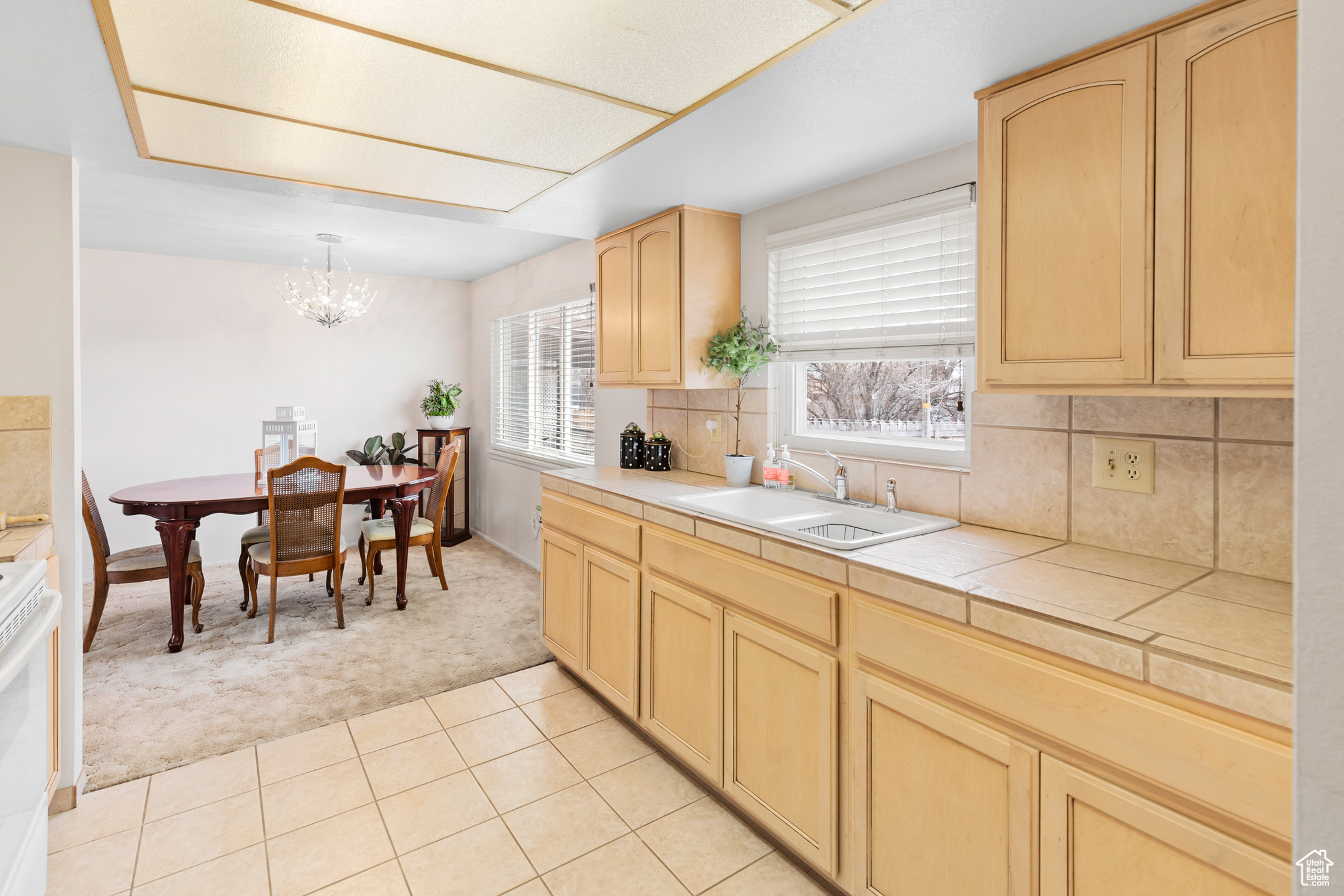 Kitchen with backsplash, sink, decorative light fixtures, light tile floors, and an inviting chandelier