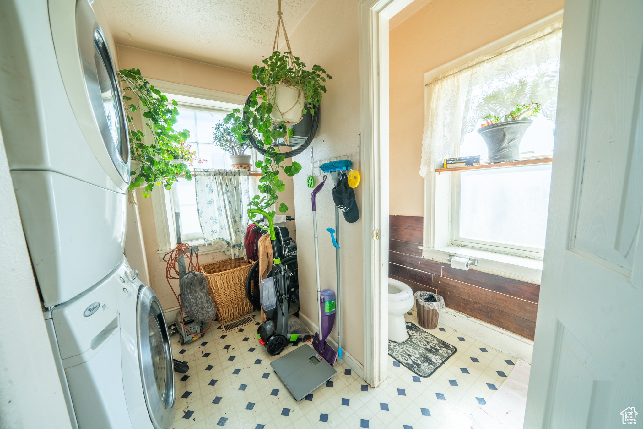 Laundry room, adjacent to half bathroom with a textured ceiling, toilet, tile flooring, and stacked washer / dryer
