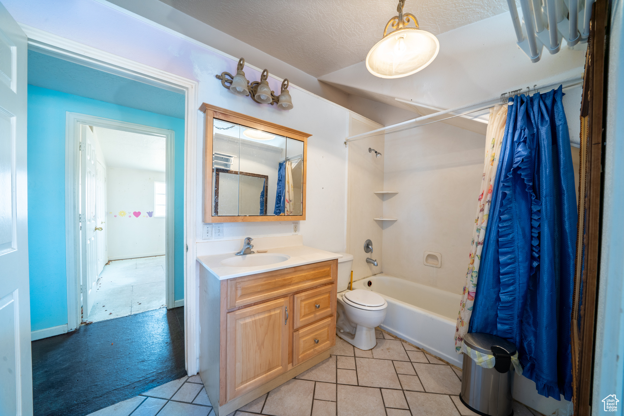 Full bathroom featuring tile floors, vanity with extensive cabinet space, toilet, a textured ceiling, and shower / tub combo with curtain