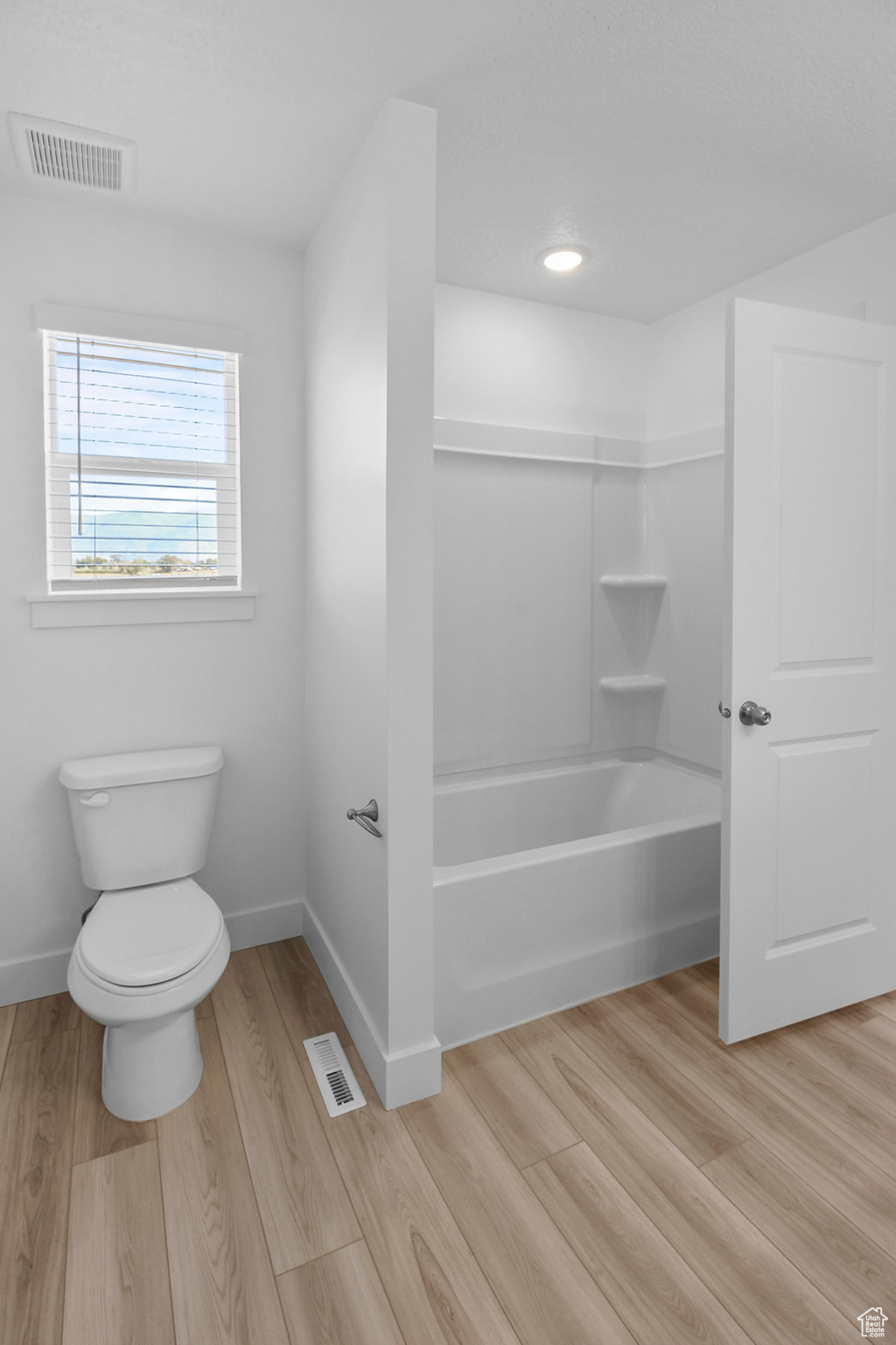 Bathroom with hardwood / wood-style floors, washtub / shower combination, and toilet