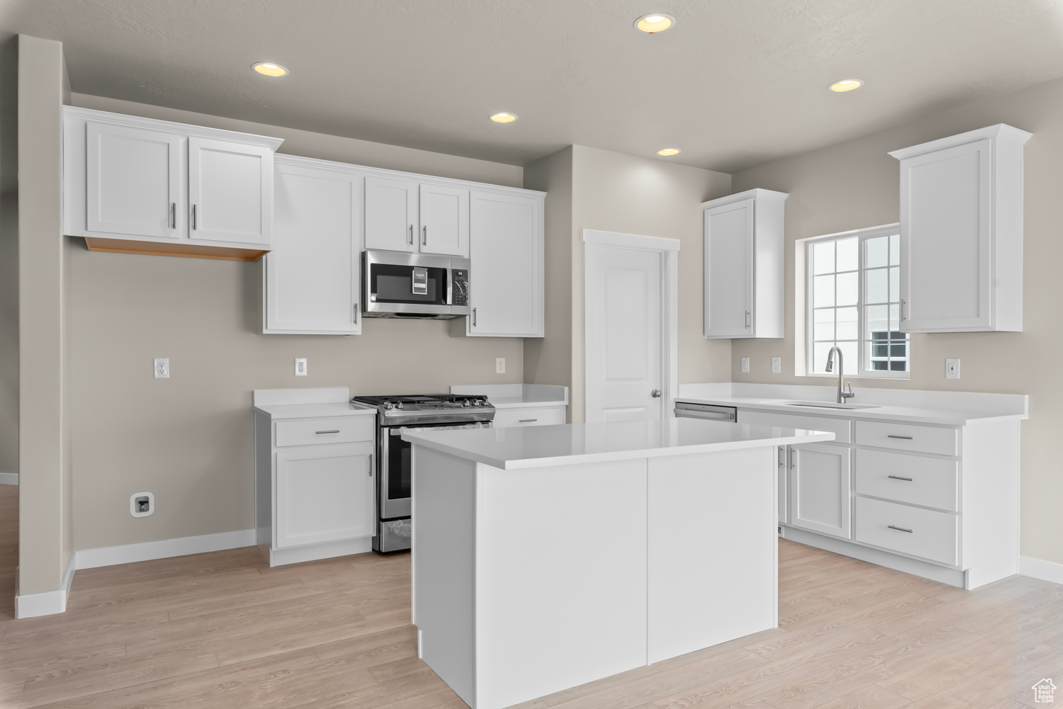 Kitchen featuring appliances with stainless steel finishes, white cabinets, sink, a center island, and light wood-type flooring