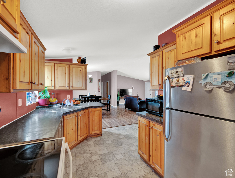 Kitchen featuring stove, sink, lofted ceiling, light tile floors, and stainless steel refrigerator