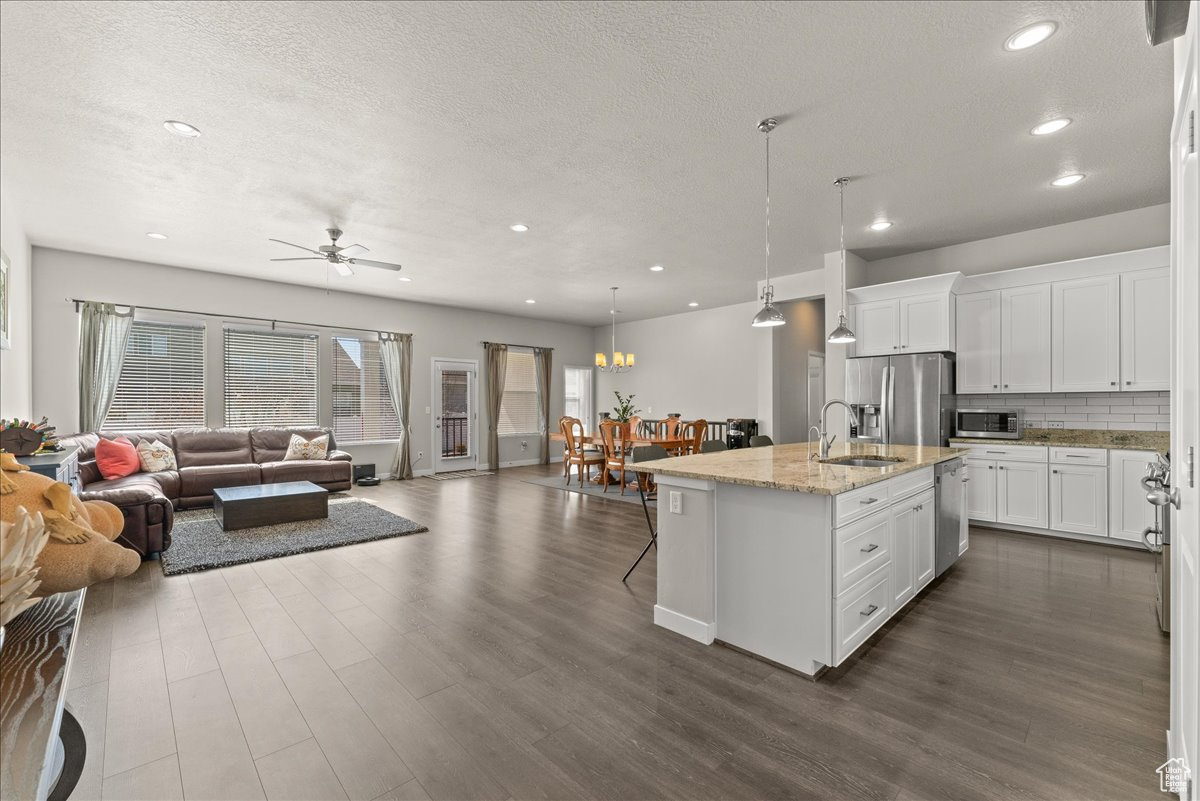 Kitchen with a kitchen island with sink, light stone counters, stainless steel appliances, decorative light fixtures, and ceiling fan with notable chandelier