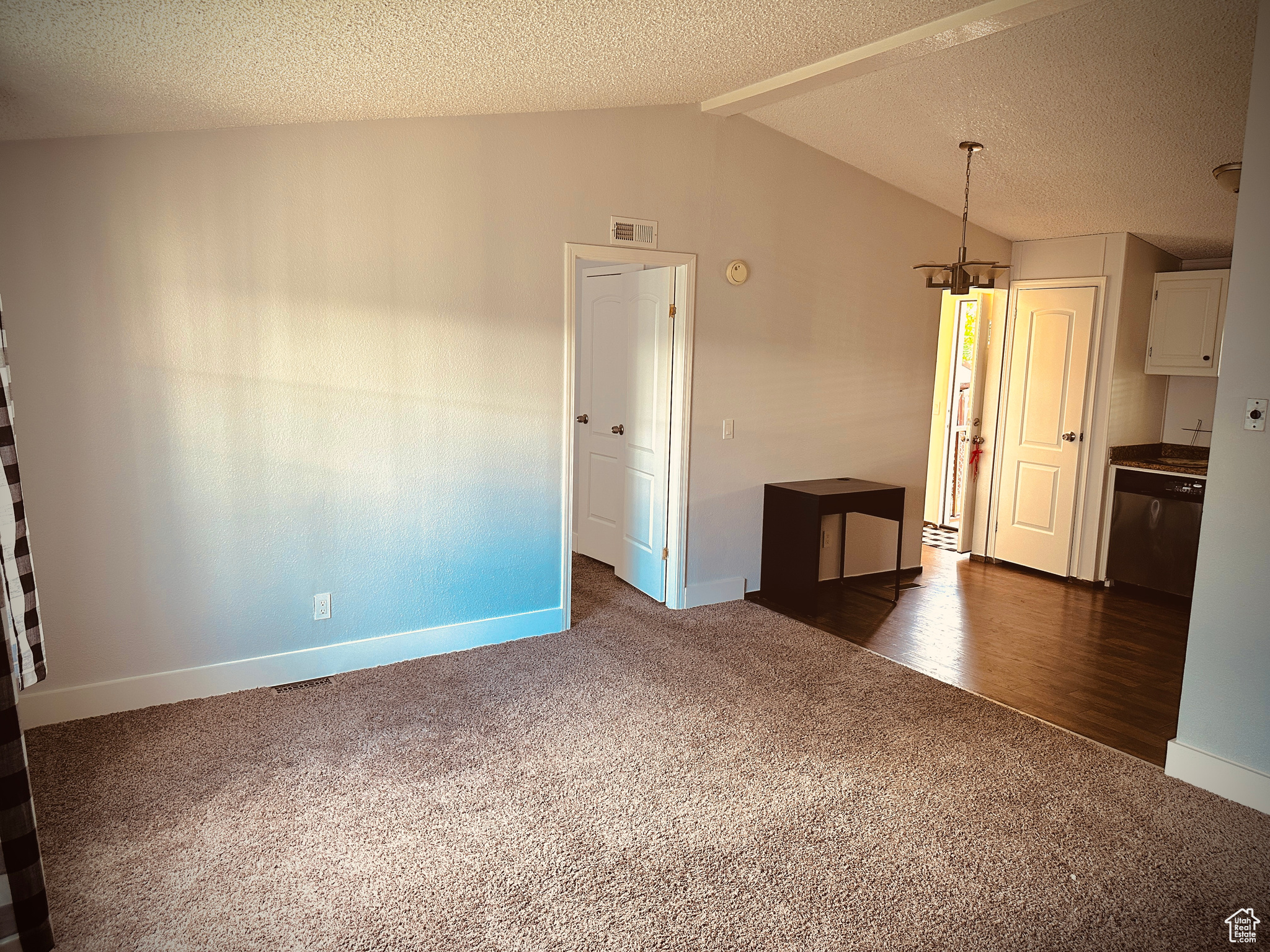 Unfurnished room with dark colored carpet, lofted ceiling, and a textured ceiling