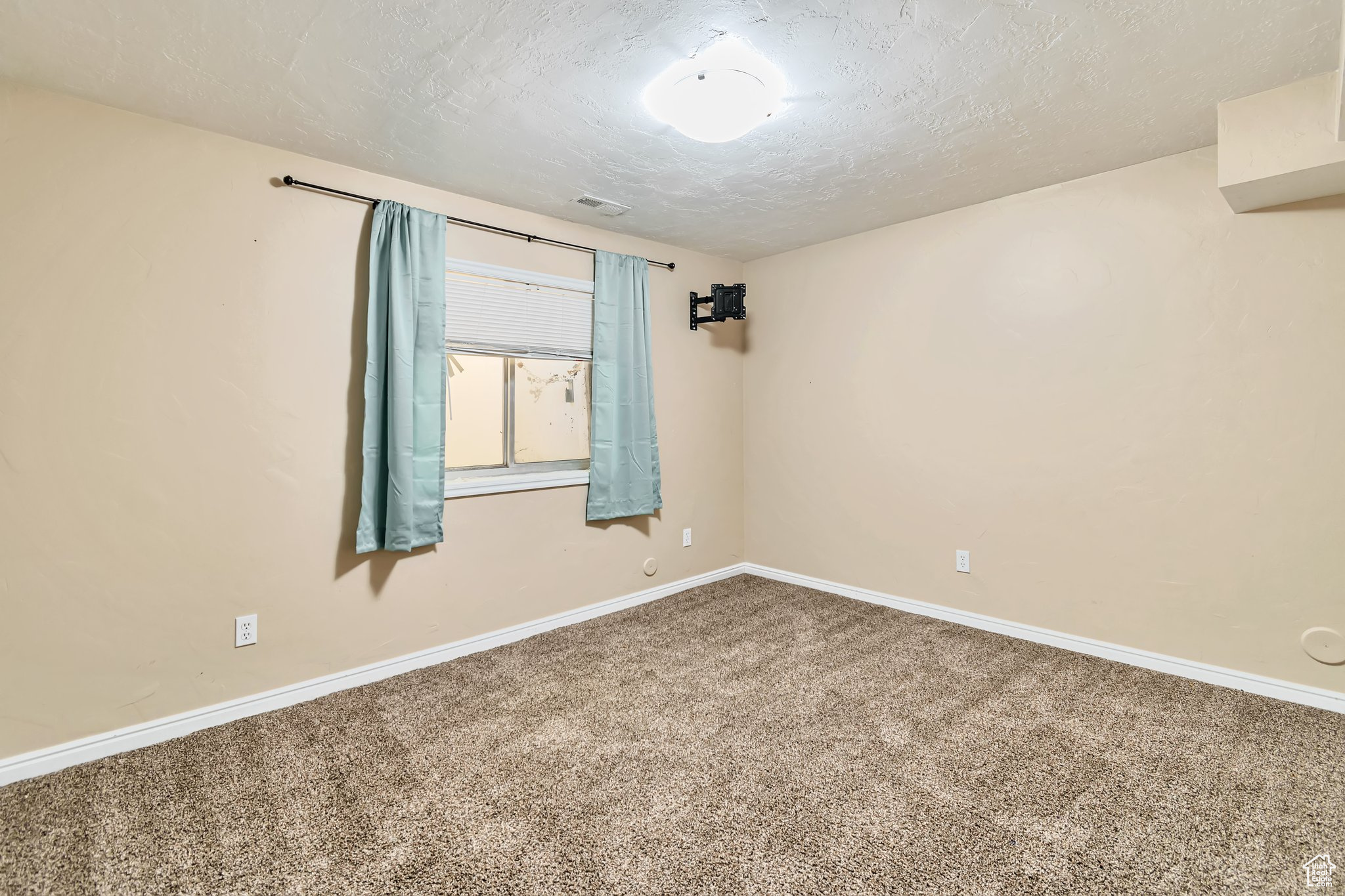 Carpeted room with window, curtains, and TV mount. textured cieling.