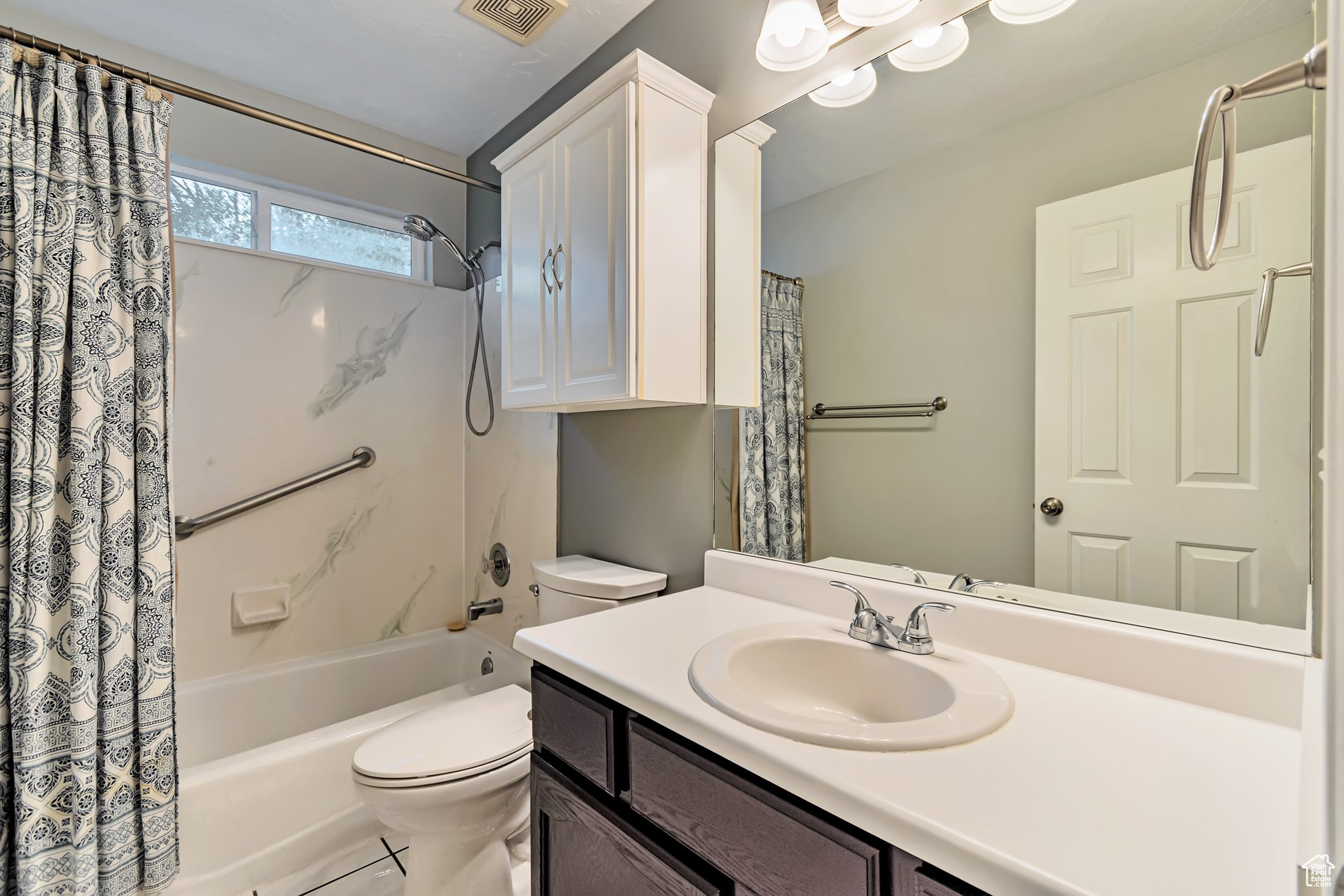 Full bathroom with large vanity, toilet, over the toilet storage, and shower / bath combo with grab bars.