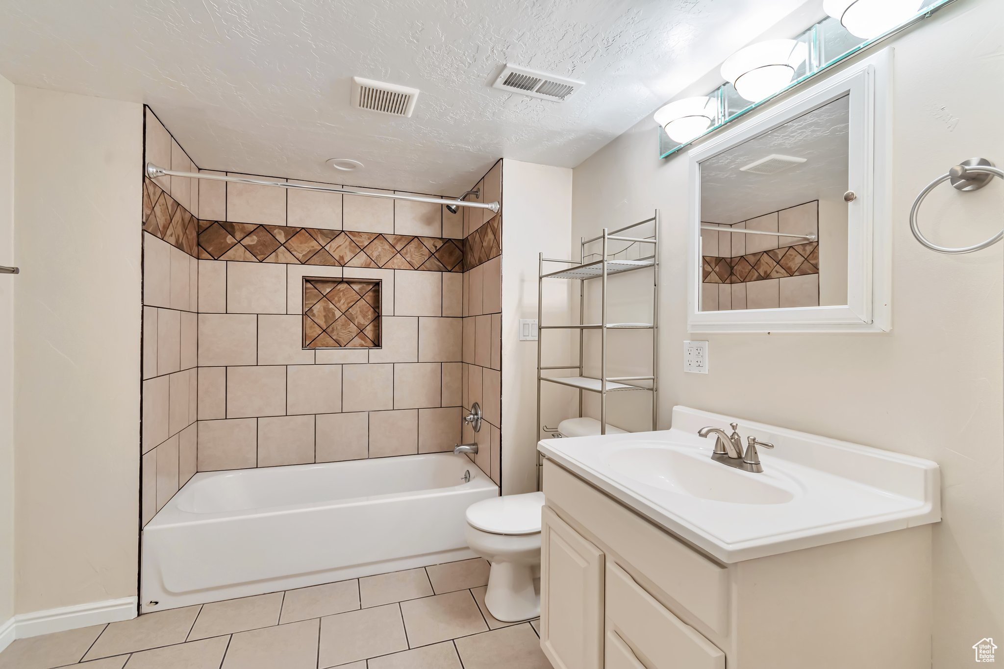 Full bathroom with tiled shower / bath combo, tile floors, toilet, over the toilet storage, mirror cabinet storage, and a textured ceiling.