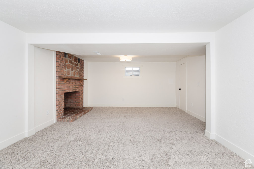 Unfurnished living room featuring a fireplace, a textured ceiling, brick wall, and light colored carpet