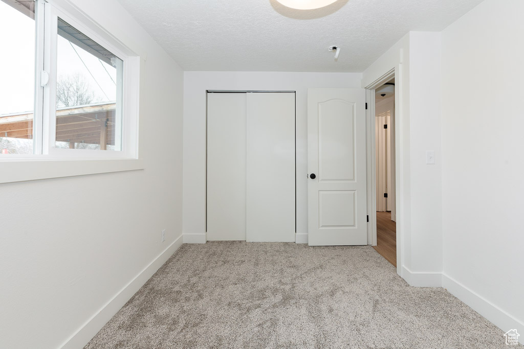 Unfurnished bedroom with a closet, light colored carpet, and a textured ceiling