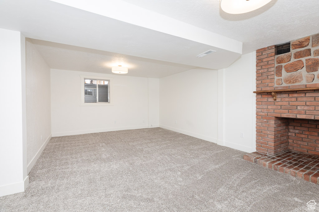 Basement featuring a brick fireplace, a textured ceiling, brick wall, and dark colored carpet