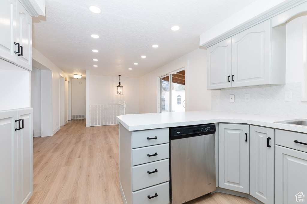 Kitchen featuring backsplash, white cabinets, dishwasher, hanging light fixtures, and light hardwood / wood-style flooring