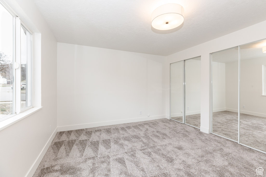 Unfurnished bedroom with multiple windows, light colored carpet, and two closets