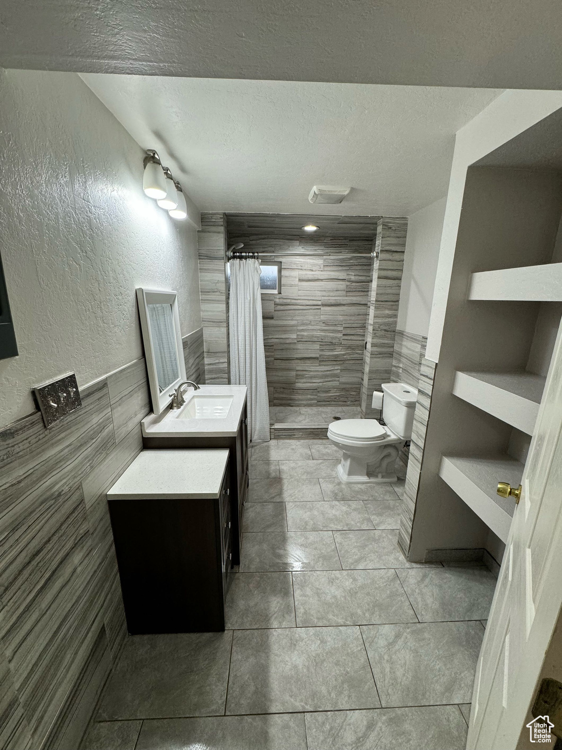 Bathroom with tile walls, tile flooring, vanity, and toilet