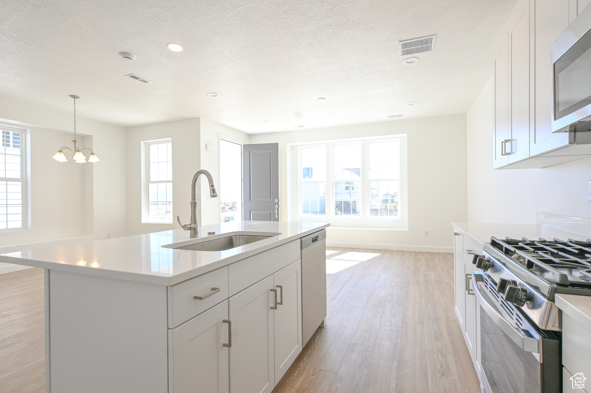 Kitchen featuring sink, appliances with stainless steel finishes, light hardwood / wood-style flooring, a center island with sink, and an inviting chandelier