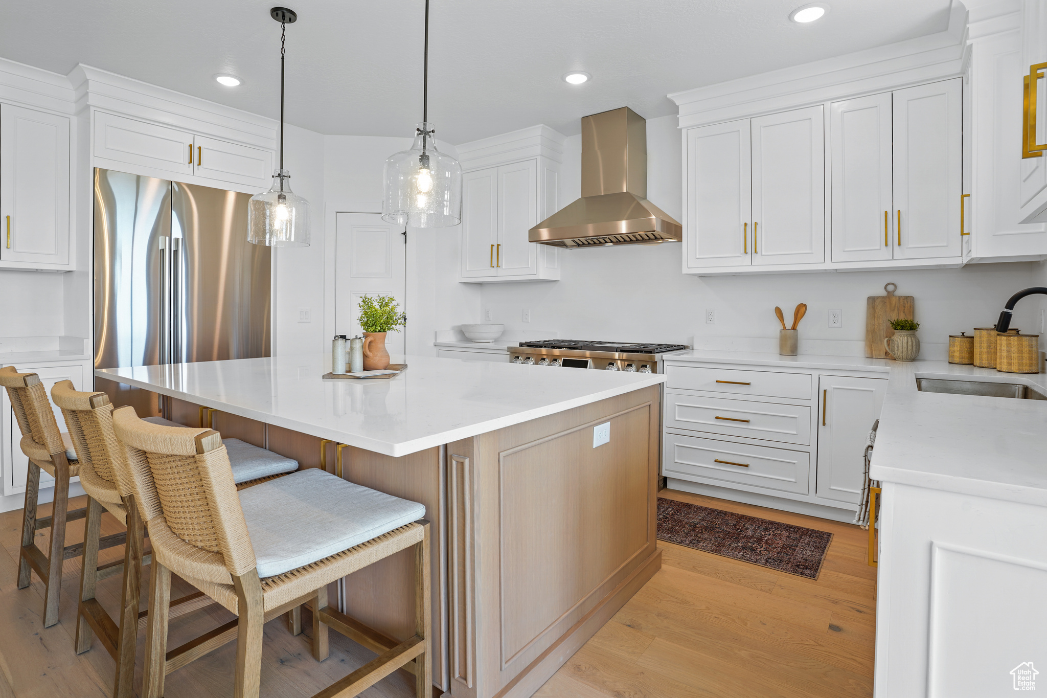 Kitchen featuring a kitchen island, stainless steel fridge, wall chimney exhaust hood, light wood-type flooring, and sink