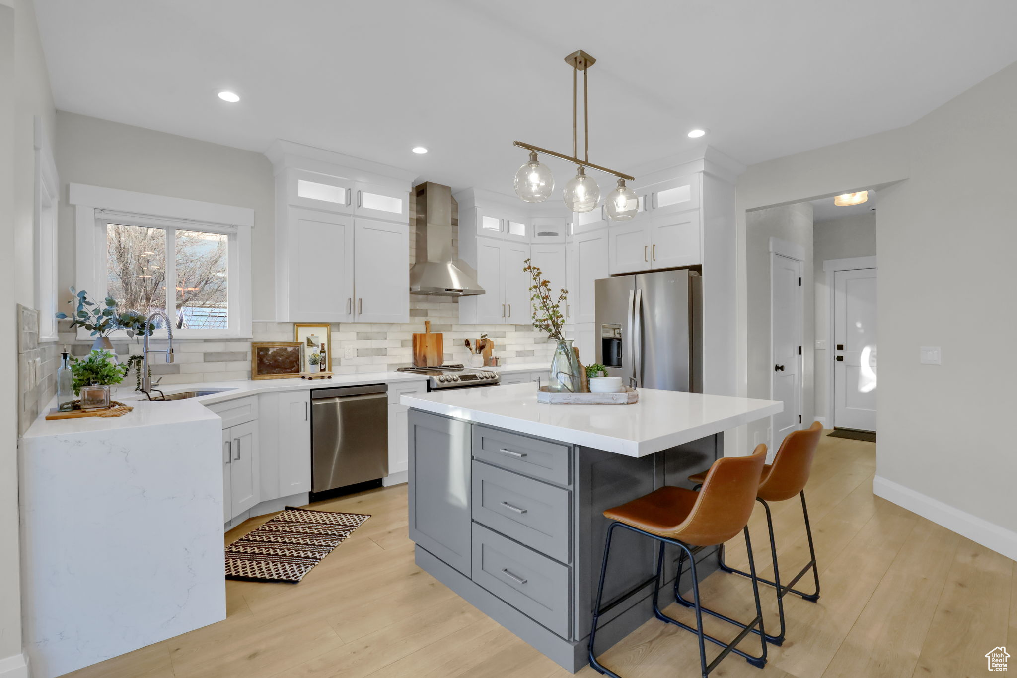 Kitchen featuring light wood-type flooring, a center island, decorative light fixtures, wall chimney exhaust hood, and appliances with stainless steel finishes